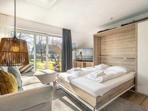 A modern bedroom with a bed, a sofa, a TV, and a large window. - 1 in the Westmarken Building (St. Peter-Ording)