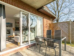 A modern outdoor patio with a glass door leading to a living area, a table with chairs, and a wooden fence. - 1 in the Westmarken Building (St. Peter-Ording)