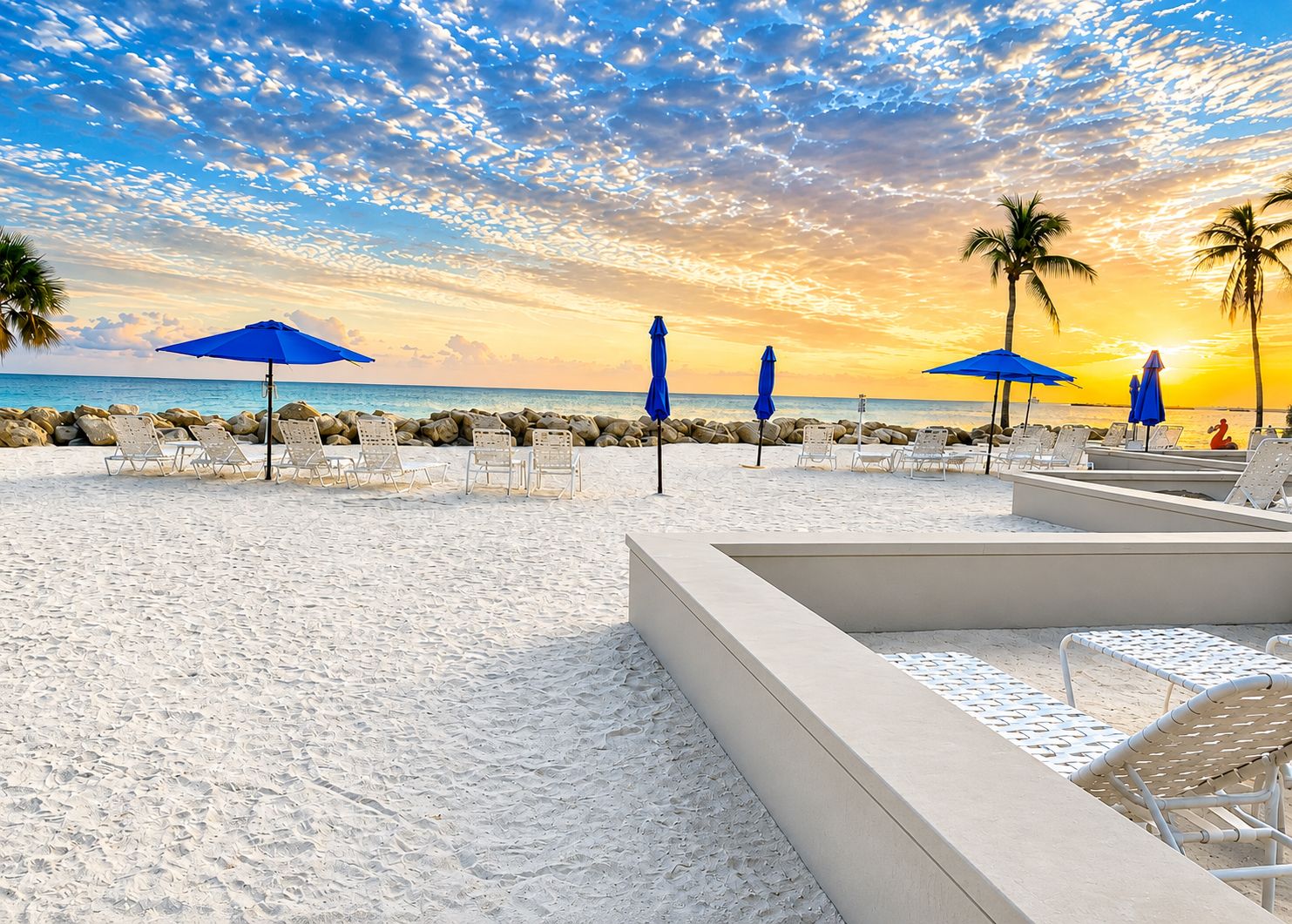 A beach resort with sun loungers and umbrellas, a clear sky, and a sunset view.