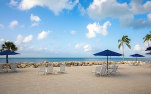 A beach with lounge chairs and umbrellas, a rocky shoreline, and palm trees. - Ocean Grand Retreat is a premiere luxury condo next to Smathers Beach (Key West)