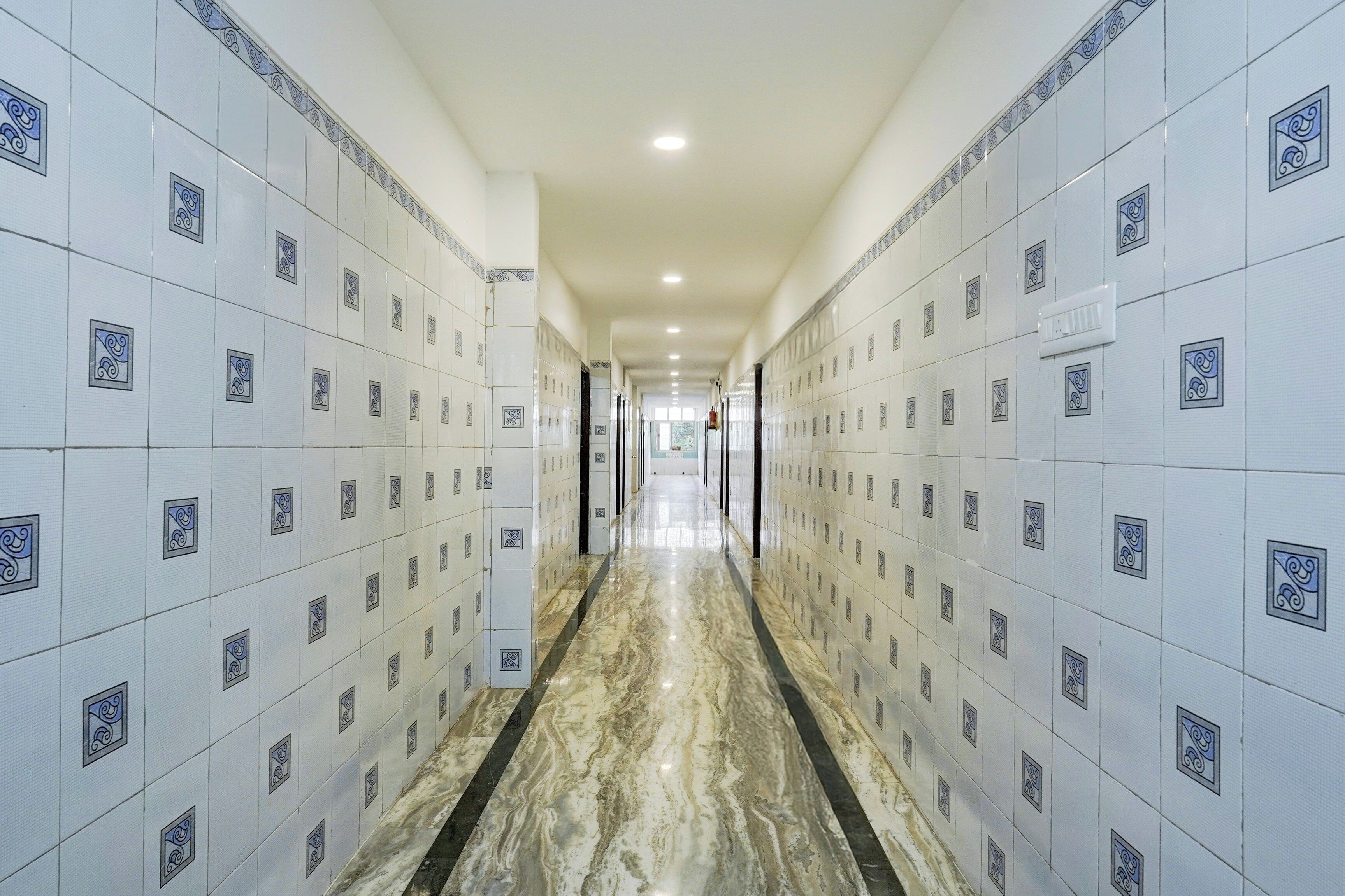 A corridor with white tiled walls and a marble floor.