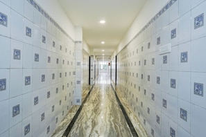 A corridor with white tiled walls and a marble floor.