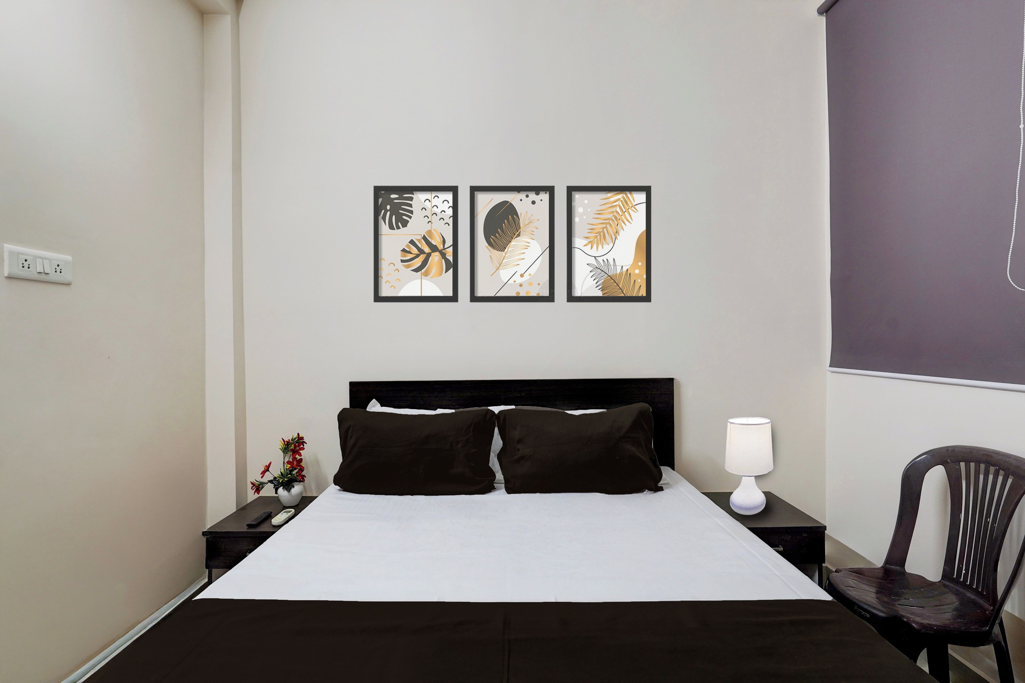 A hotel room with a bed, a nightstand, a chair, and three framed artworks on the wall.