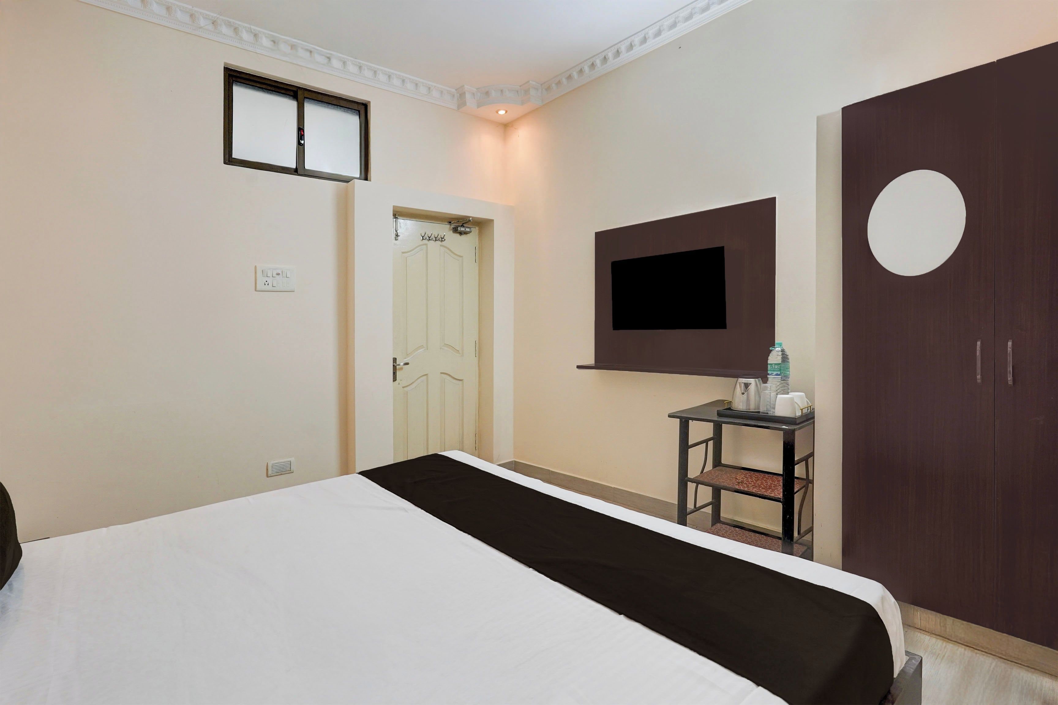 Habitación de hotel con una cama, televisor montado en la pared, armario y una mesita con una botella de agua.