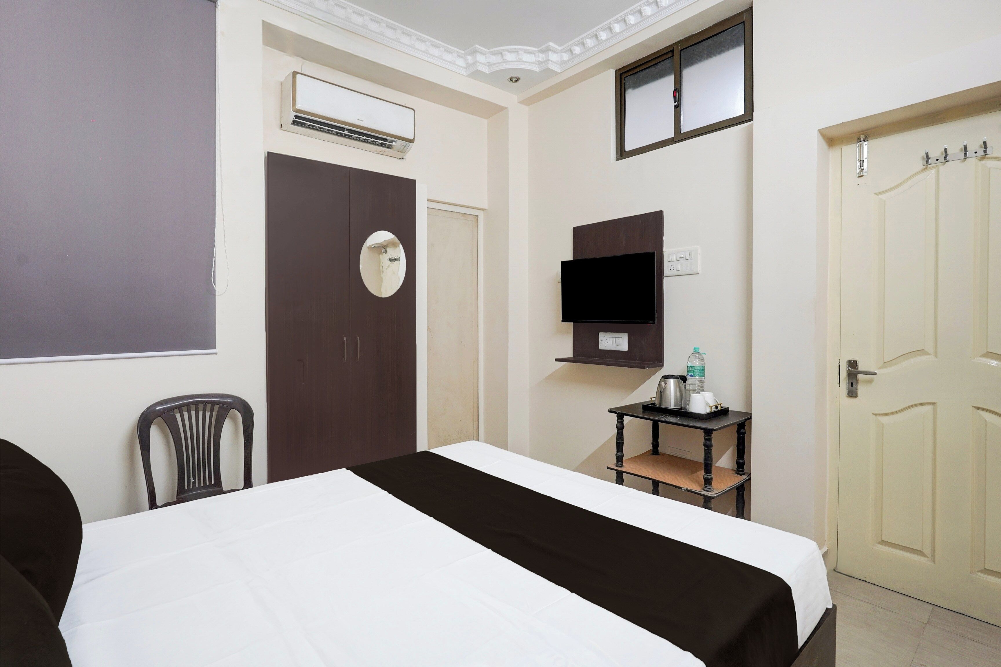 A hotel room with a bed, a desk, a chair, an air conditioning unit, a television, and a door.