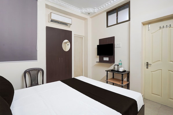 A hotel room with a bed, a desk, a chair, an air conditioning unit, a television, and a door.