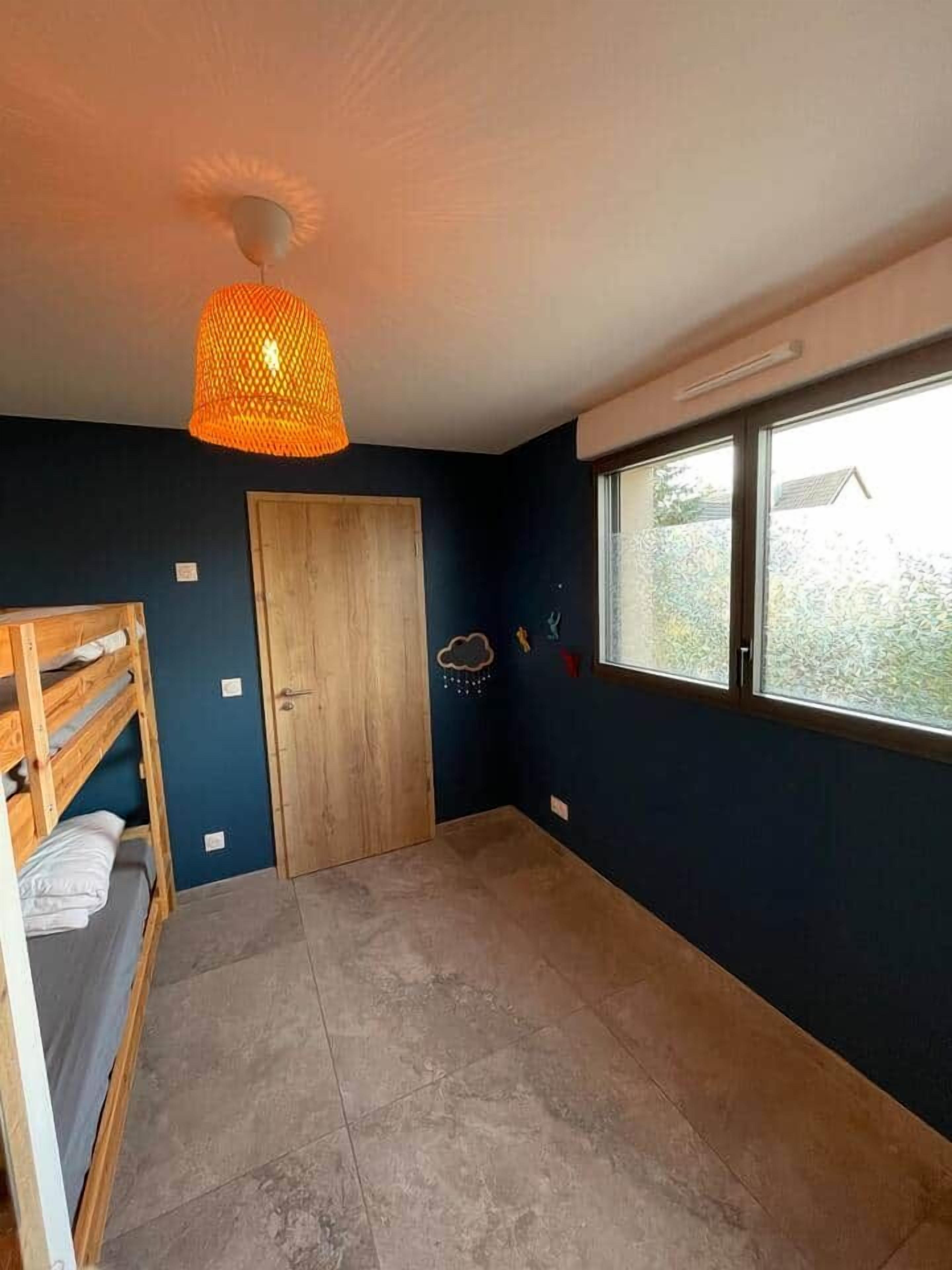 Una stanza con un letto a castello, una porta in legno, una finestra vista e un lampadario.