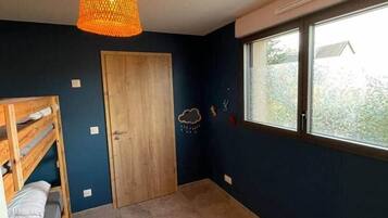 Una stanza con un letto a castello, una porta in legno, una finestra vista e un lampadario.