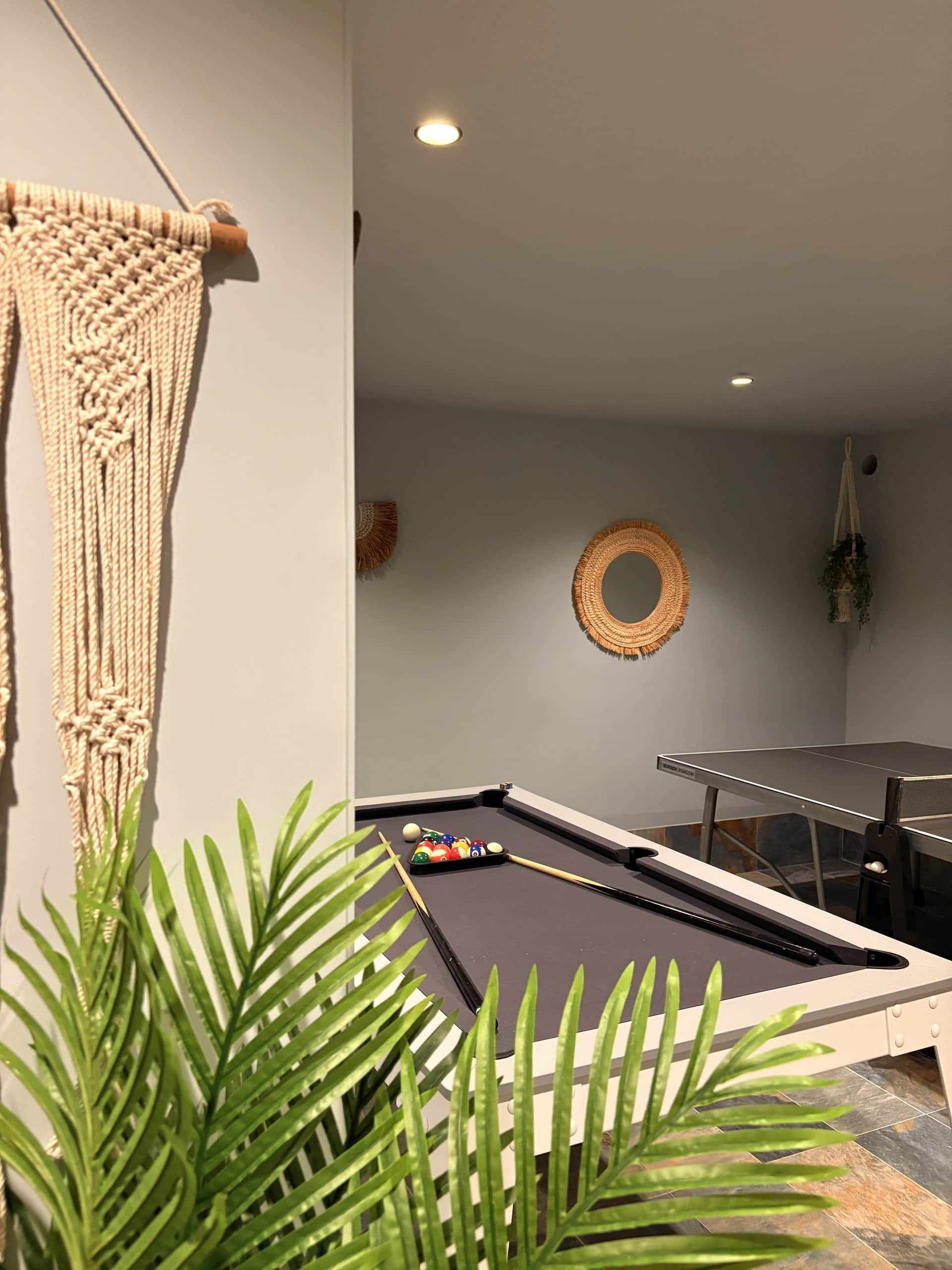 A pool table with a set of billiard balls, a macrame wall hanging, and a round woven decoration.