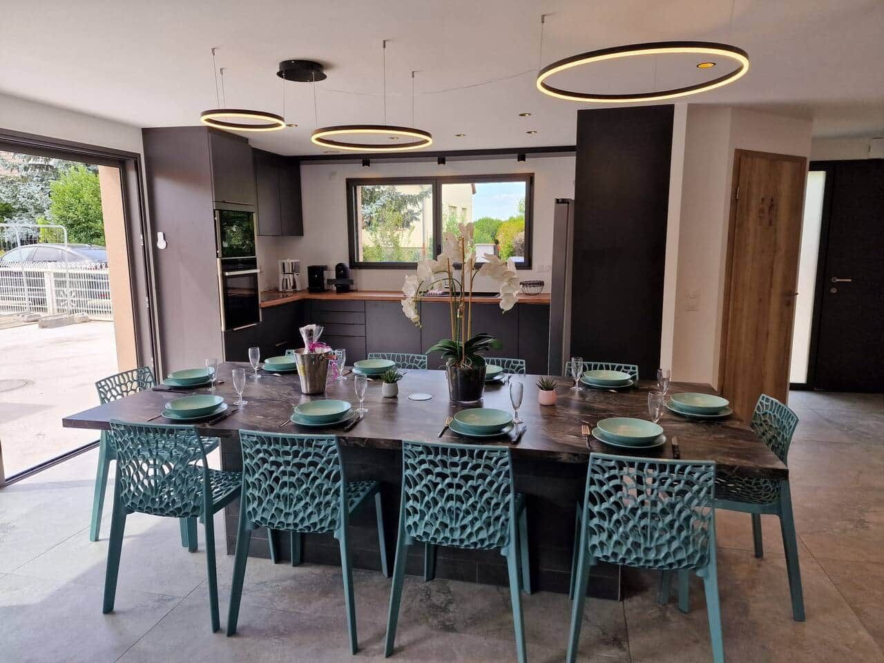 Un espace de salle à manger moderne, avec une table rectangulaire dressée pour six personnes, entourée de six chaises dont les dossiers présentent des motifs complexes.