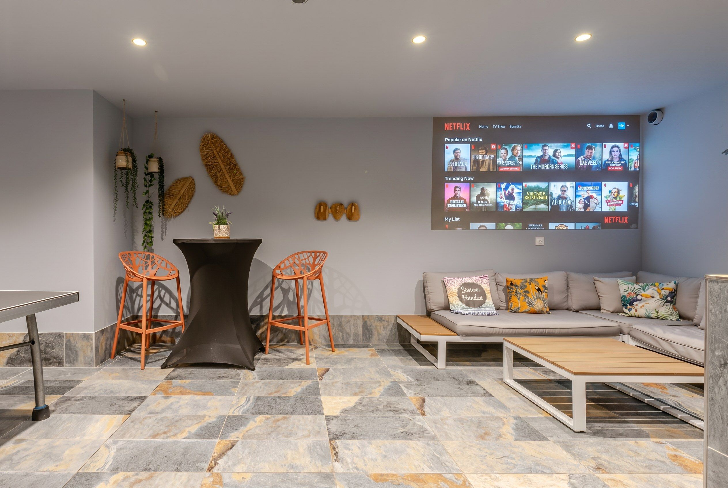 Un salon moderne comprenant un canapé, deux fauteuils, une table basse et un téléviseur fixé au mur qui affiche l’interface de Netflix.
