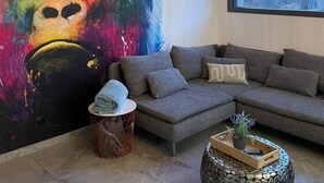En stue med et stort abstrakt billede, en moderne sofa, et rundt sofabord i sten og en hængende lampe.