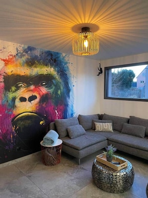 Een woonkamer met een groot abstract schilderij, een moderne bank, een ronde steen koffietafel en een hanglamp.