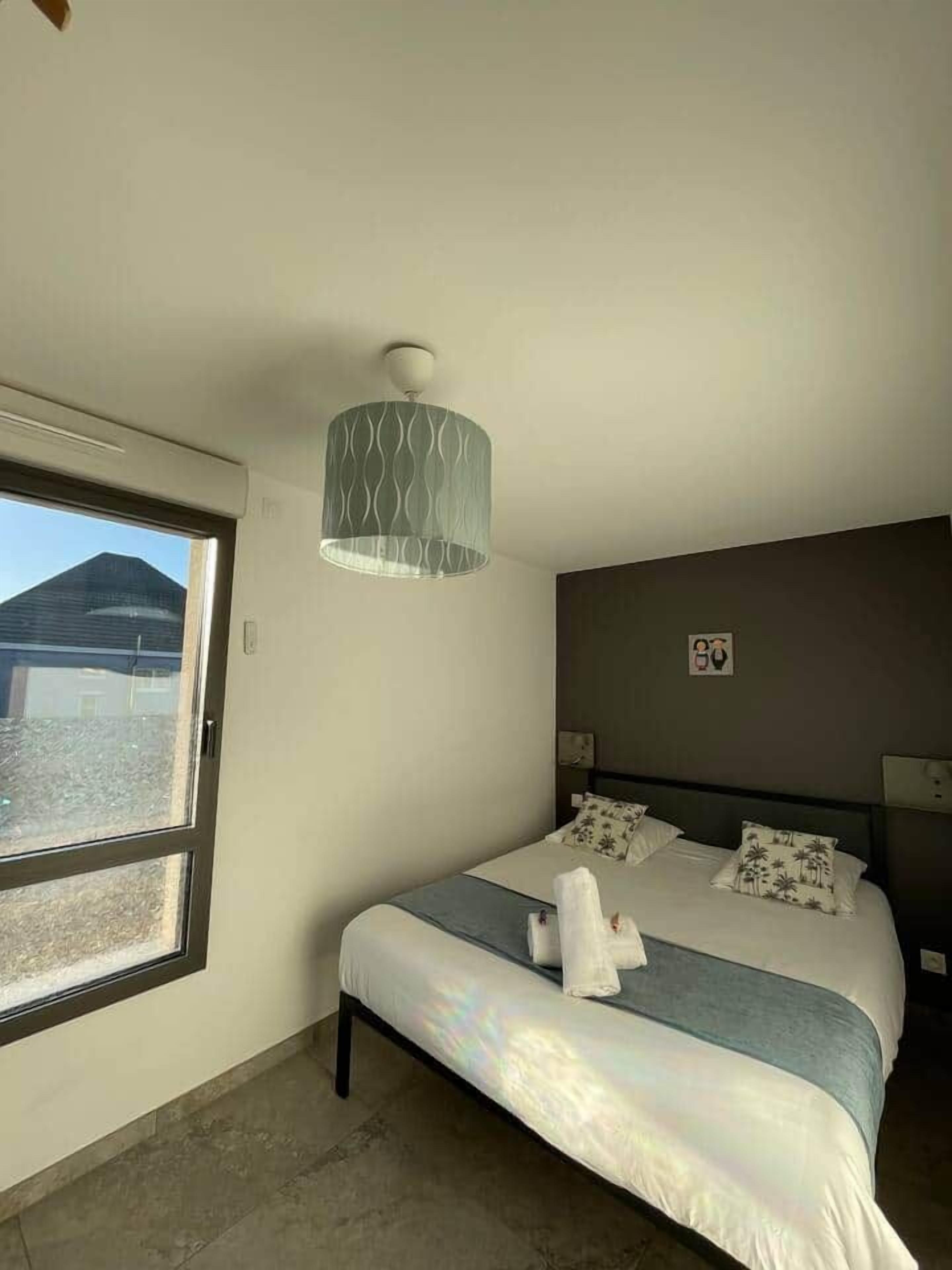 Une chambre d’hôtel avec un lit, une fenêtre, un luminaire fixé au mur et une couvre-lit.