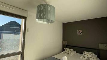Une chambre d’hôtel avec un lit, une fenêtre, un luminaire fixé au mur et une couvre-lit.