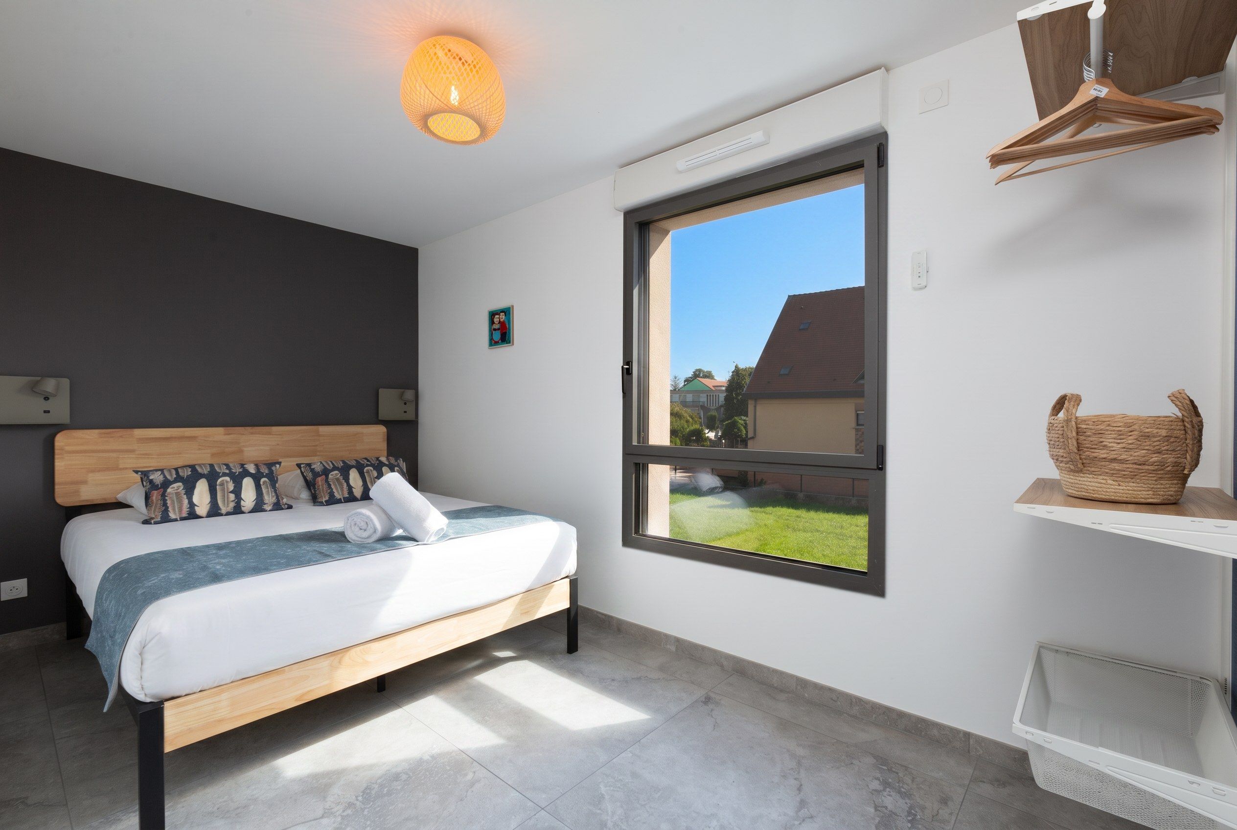 Ein modernes Schlafzimmer mit einem großen Fenster, einem Bett mit Holz-Kopfteil und einem kleinen Gemälde an der Wand.