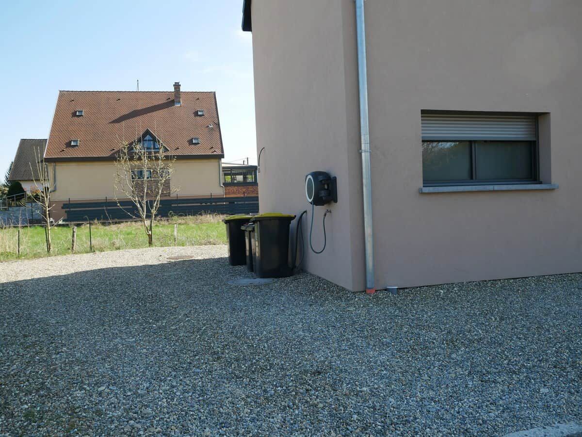 Un bâtiment avec une allée gravillonnée, une poubelle et une fenêtre dont le volet est fermé.