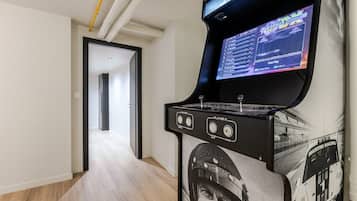 Een gameconsole met een beeldscherm waarop een racegame draait, in een hal met een houten vloer en een deur naar een andere kamer.
