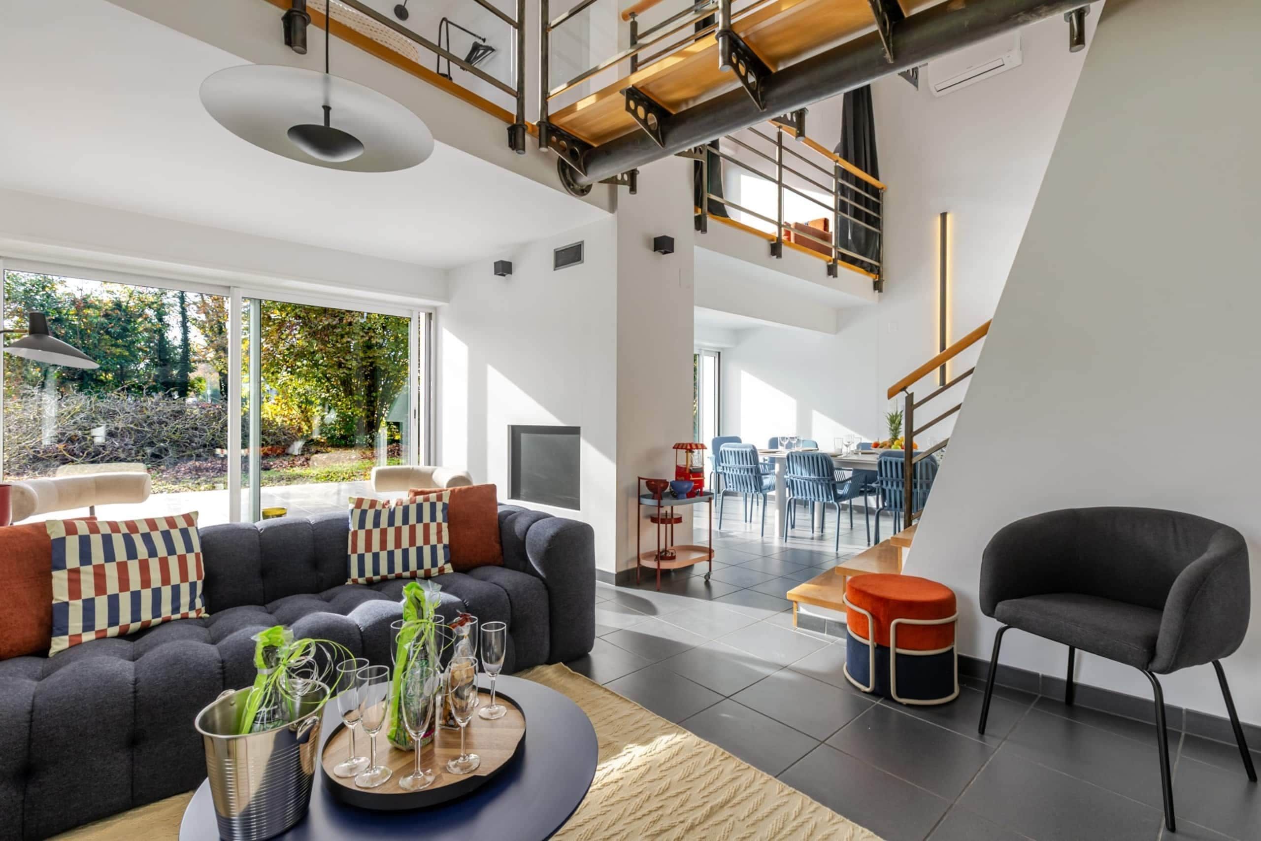 A modern living room with a sofa, chairs, and a dining area with a staircase.