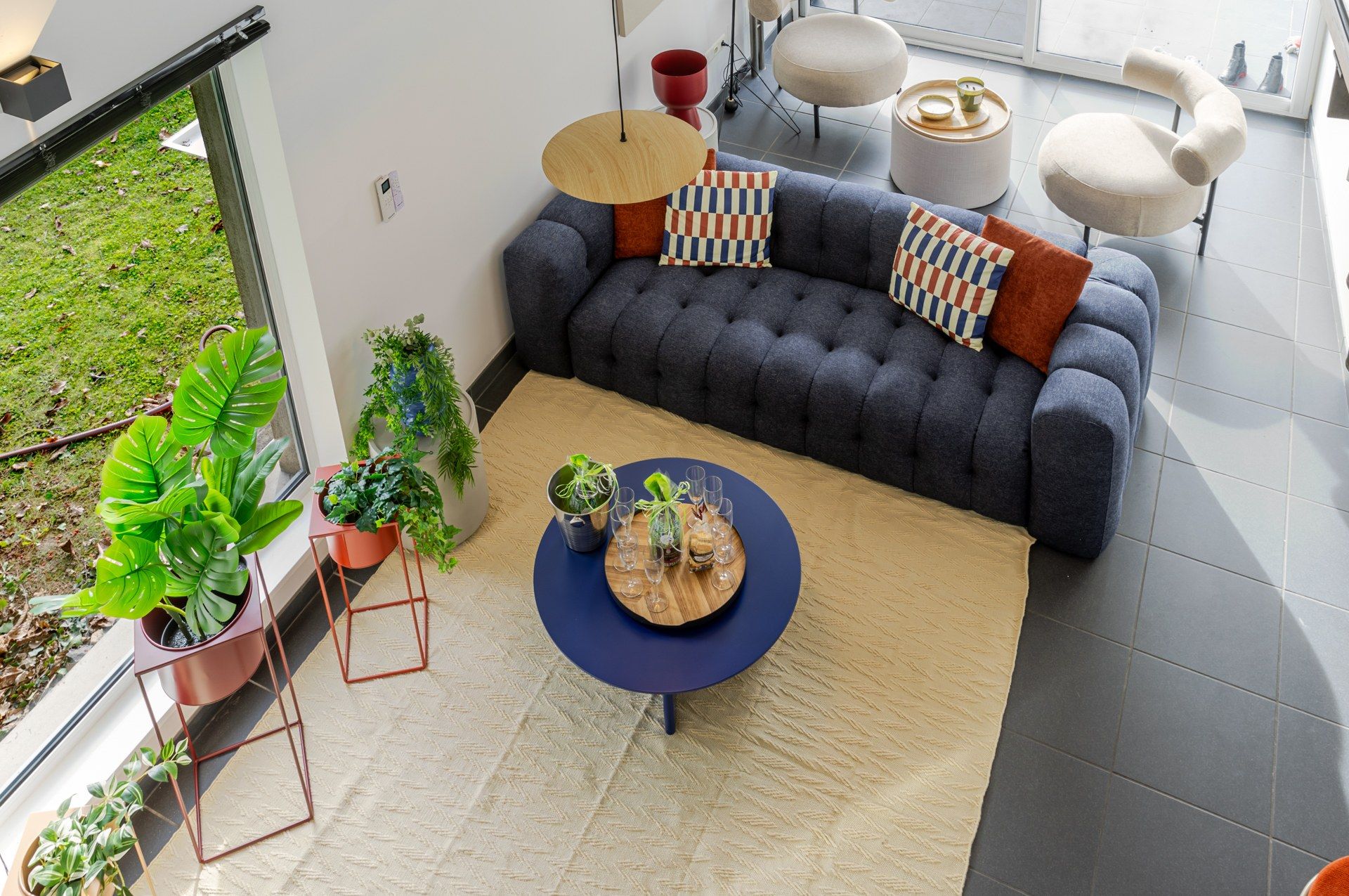En moderne stue med en mørkegrå sofa, mønstrede puder, et rundt sofabord og krukkeplanter.