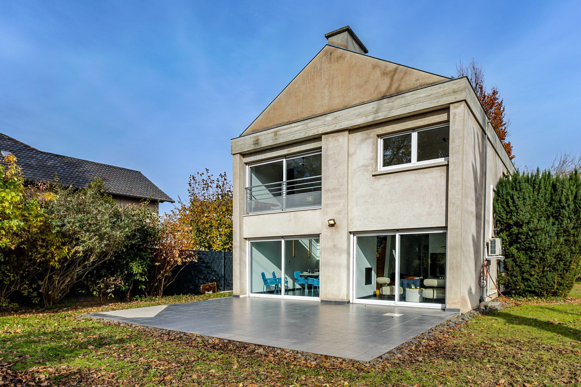 A modern two-story house with a flat roof, large windows, and a covered patio area.
