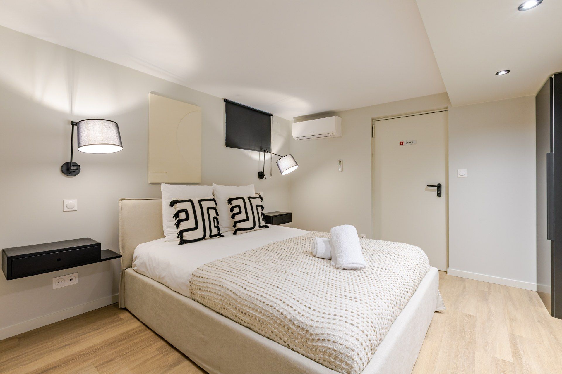 Een moderne hotelkamer met een bed, nachtkastjes, een aan de muur bevestigde televisie en een deur met privacyvergrendeling.