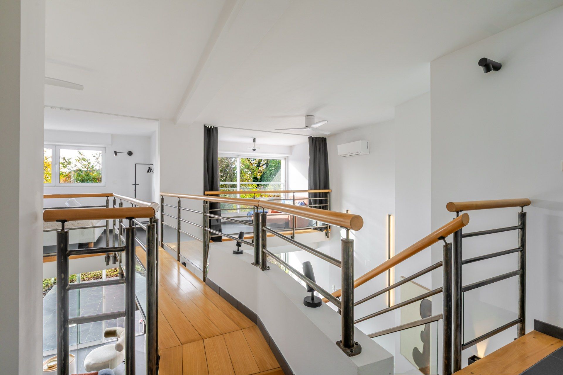 Een modern interieur met een houten trap, glazen balustrades en uitzicht op de omgeving.
