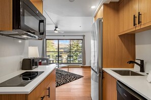 A modern kitchen with a built-in microwave, stove, and refrigerator, a dining area with chairs, and a large window offering a view of the outdoors. - Beaver Run|Ski In/Out|Cozy Chalet|Pool & Hot Tub (Breckenridge)