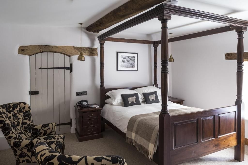 Una cama con dosel, cabecera de madera, mesita de noche, una silla y una puerta con arco rústico.