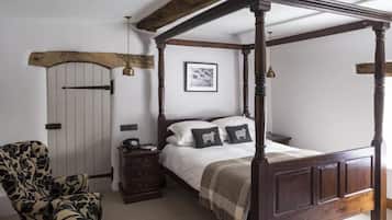 A four-poster bed with a wooden headboard, a nightstand, a chair, and a door with a rustic arch.