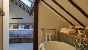 A bedroom with a bed, a bathroom with a bathtub, and a skylight. - Tudor Farmhouse Hotel (Clearwell)