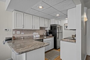 A modern kitchen with white cabinets, granite countertops, a stainless steel refrigerator, and a built-in oven. - Beaver Run -Breck Blast|Ski Views|Pool&Hot Tubs (Breckenridge)