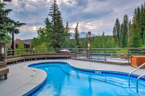 A swimming pool with a curved design, surrounded by a wooden deck and metal railings. - Beaver Run -Breck Blast|Ski Views|Pool&Hot Tubs (Breckenridge)