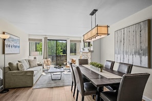 A spacious living area with a dining table, comfortable seating, a fireplace, and a large window offering a view of the outdoors. - Beaver Run - Breck Blast|Ski Views|Pool&Hot Tubs (Breckenridge)