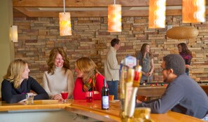 A group of people seated at a wooden table in a brick-walled room with hanging pendant lights. - Beaver Run -Our Happy Place | Luxury Suite (Breckenridge)