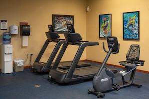 Ein Fitnessraum mit Laufbändern, einem Ergometer, einem Wasserspender und einem Papierkorb.