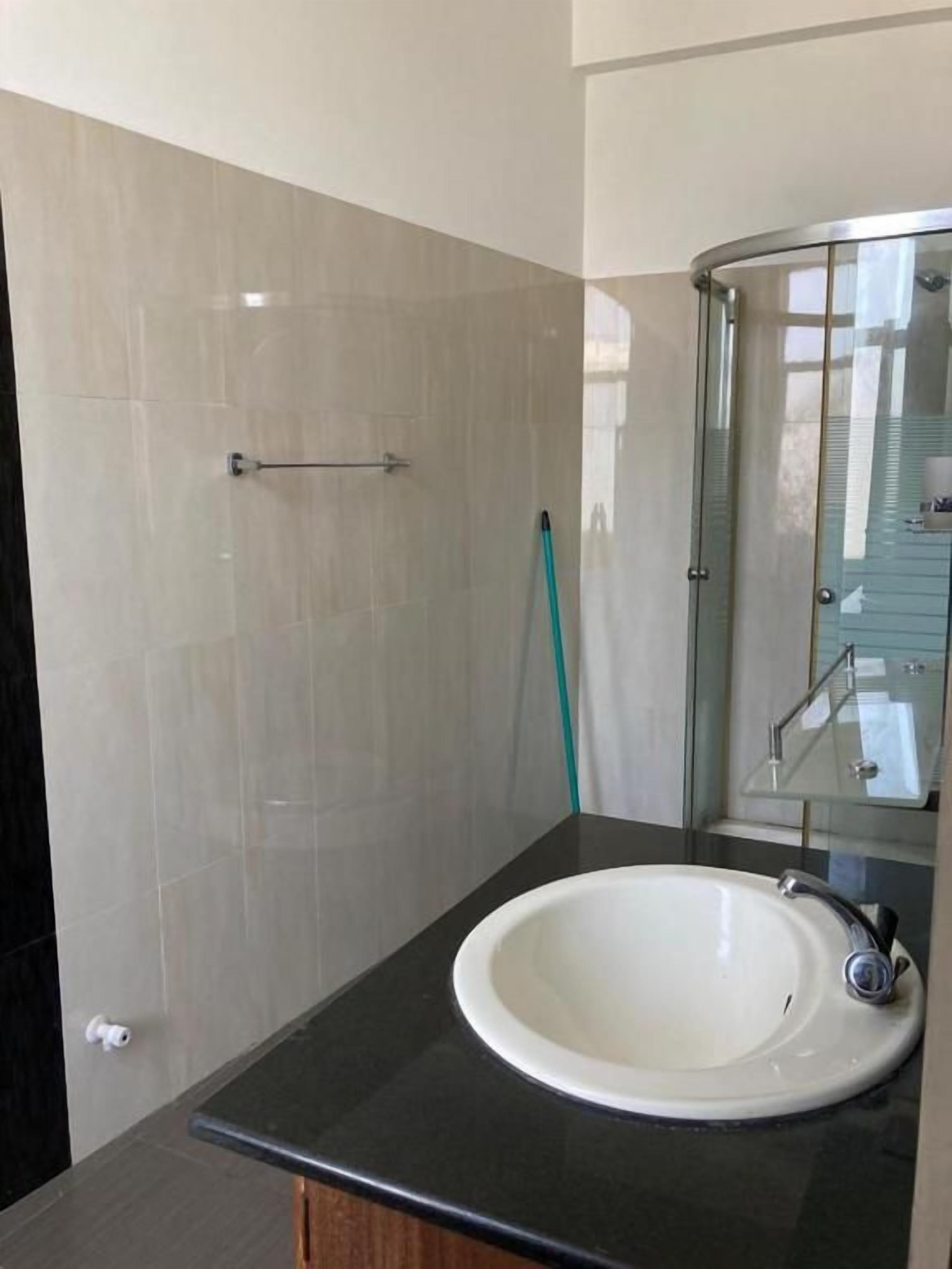 Un baño con lavamanos blanco, cabina de ducha con mampara de vidrio y espejo.