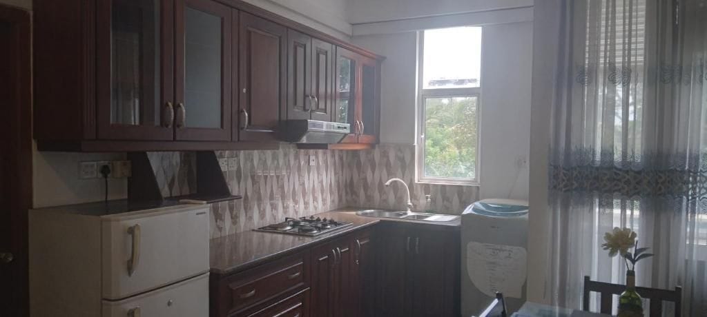A kitchen with wooden cabinets, a stove, a sink, and a window with curtains.