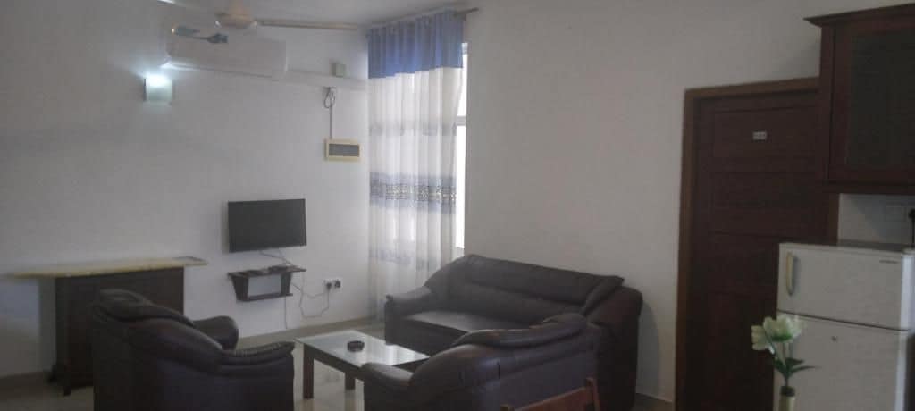 A living room with a sofa, a small table, a TV, and a refrigerator.