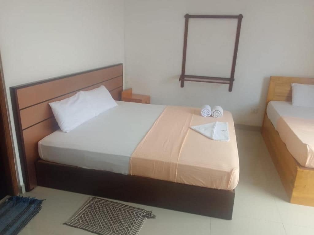 A hotel room with two beds, a small table, and a wall-mounted shelf.