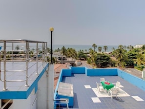 A rooftop terrace with a view of the sea, a table with chairs, and a lamp post.