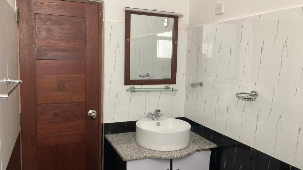 Une salle de bain avec une porte en bois, un lavabo blanc, une étagère en verre et un miroir.
