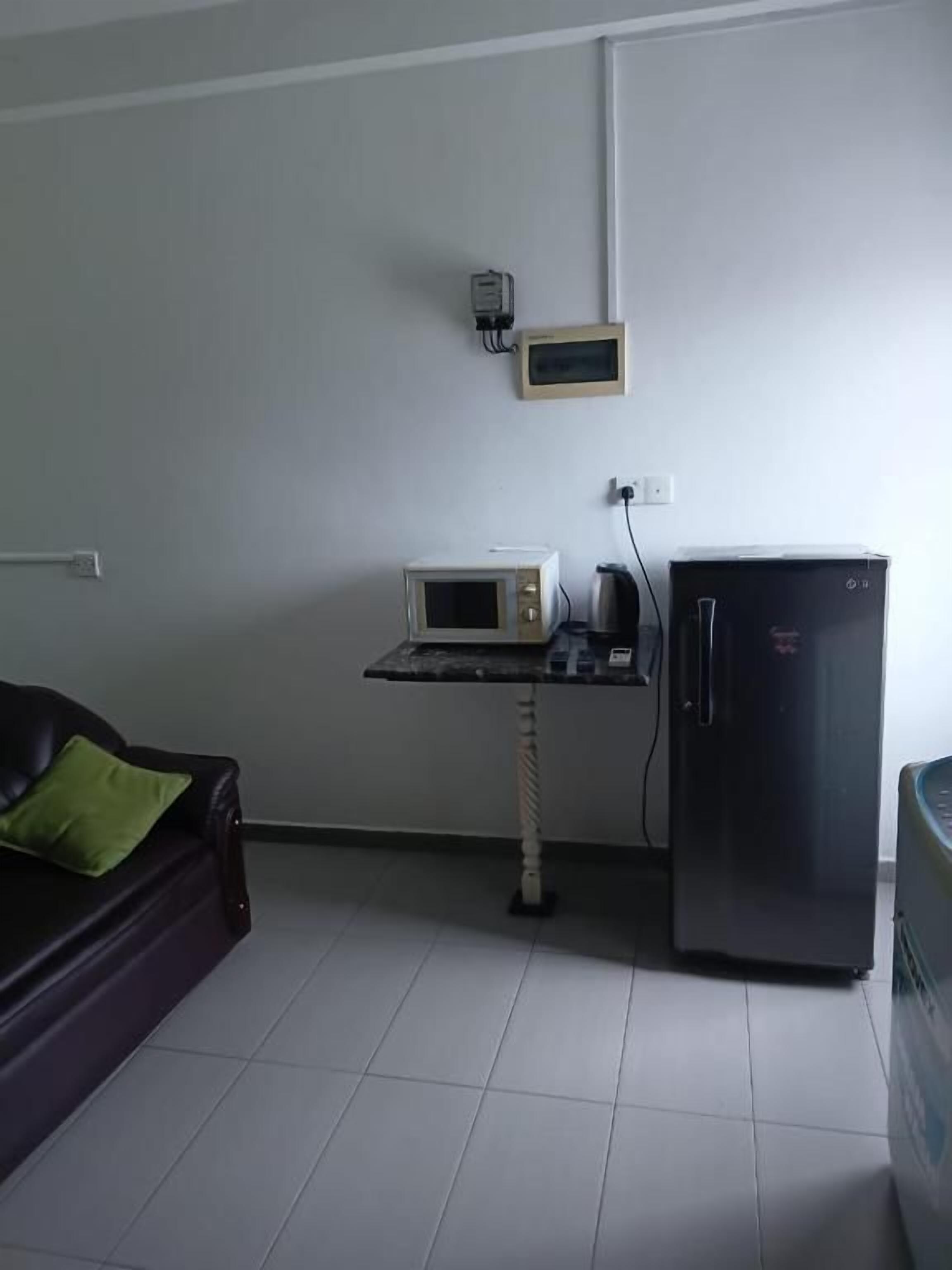 A room with a black refrigerator, a microwave on a small table, and a couch with a green pillow.
