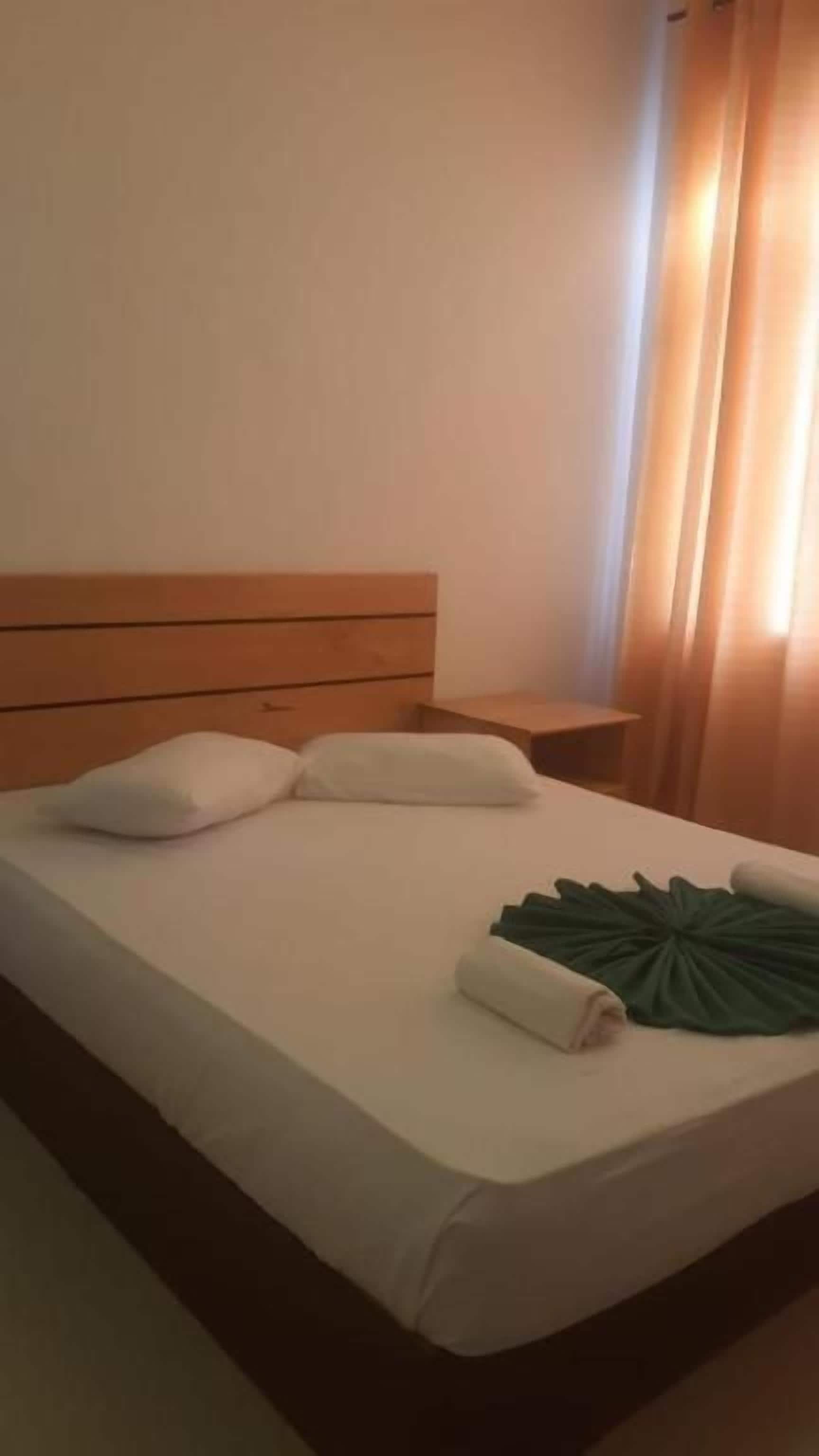 A hotel room with a wooden headboard, a bed with white linens, and a green leaf-shaped pillow.
