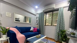 Una sala de estar con un sofá azul, una mesita, una planta en maceta y una ventana con cortinas.