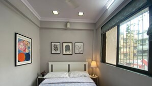 Una habitación de hotel con una cama, una mesita de noche, una lámpara y tres láminas botánicas enmarcadas en la pared.