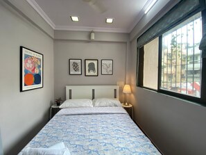 Ett hotellrum med en säng, ett nattduksbord, en lampa och tre inramade botaniska illustrationer på väggen.