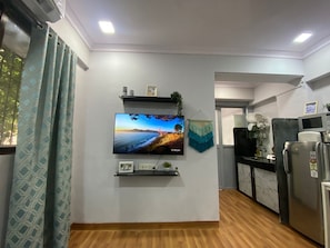 A modern kitchen with a flat-screen TV mounted on the wall, a refrigerator, and a microwave.