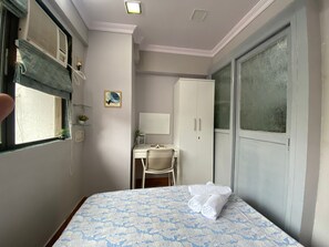 Ett hotellrum med en säng, ett skrivbord, en stol, en garderob och ett fönster med persienner.