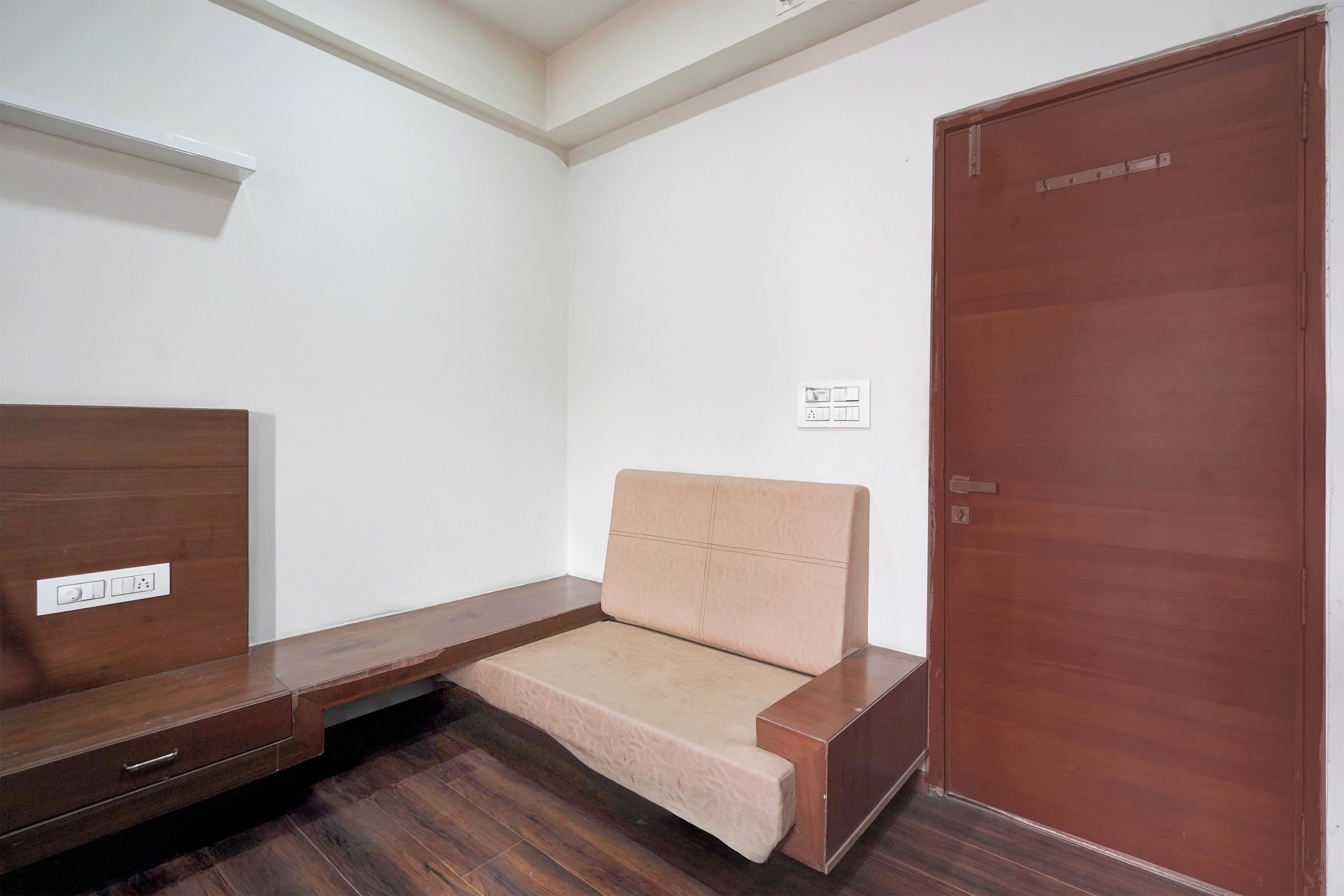 Ein Zimmer mit einer Holzbank, einem kleinen Sofa, einer Holztür und einer weißen Wand mit Lichtschalter.